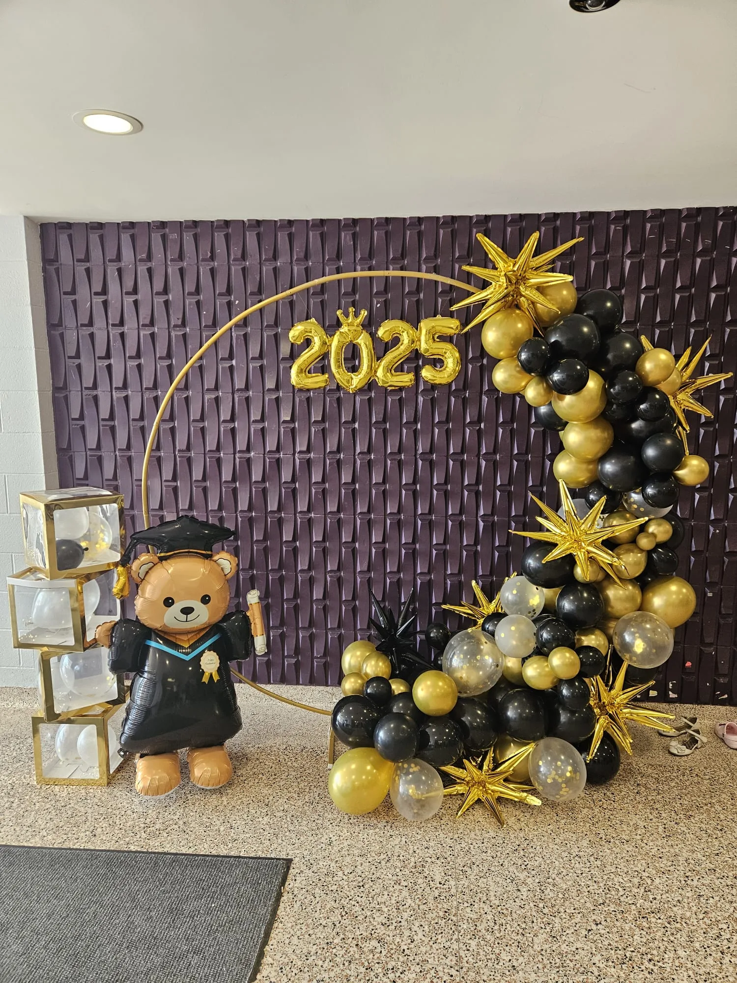 Black and gold balloon hoop arch with 2025 foil numbers and grad bear backdrop