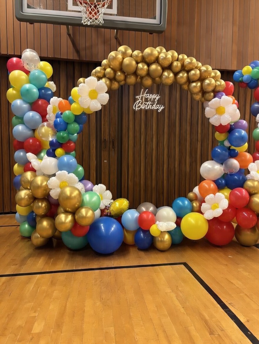 Rainbow primary-color balloon frame with daisies in a school gym